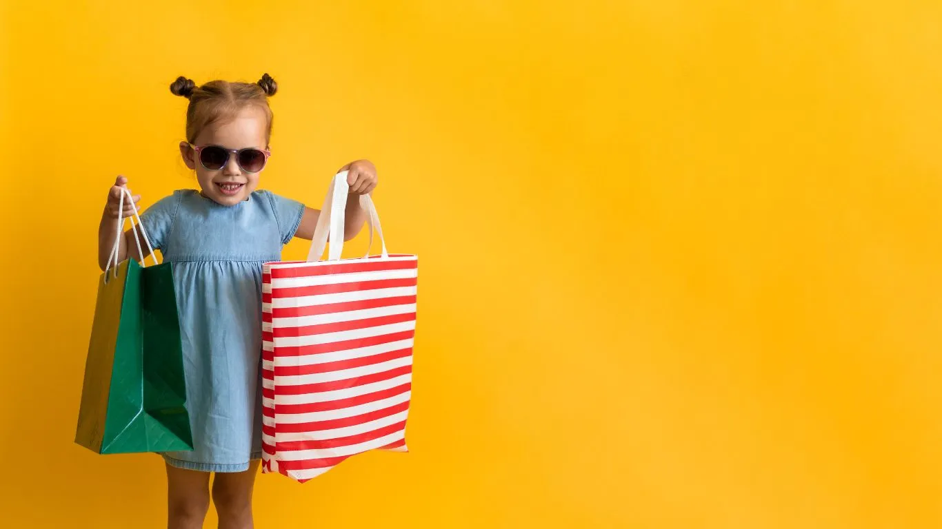 Anak kecil membawa dua tas belanja di depan latar kuning